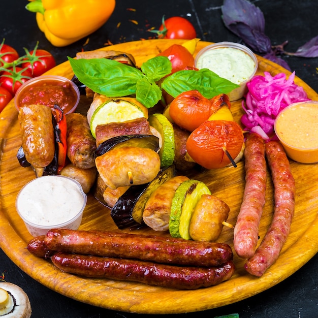 Hot browned ruddy homemade sausages on a wooden tray with sauces and vegetables