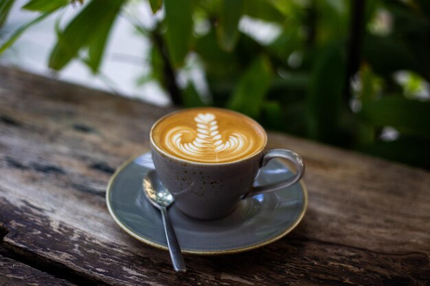 カフェの茶色の古い木製のテーブルにハート型のラテアートとホットカプチーノコーヒーカップ