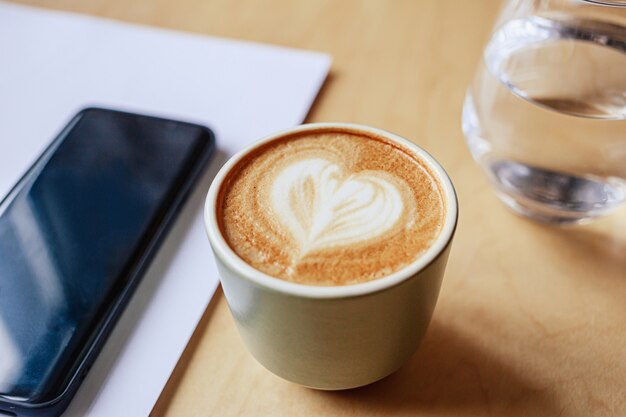 Hot cappuccino on the table and phone on wooden table