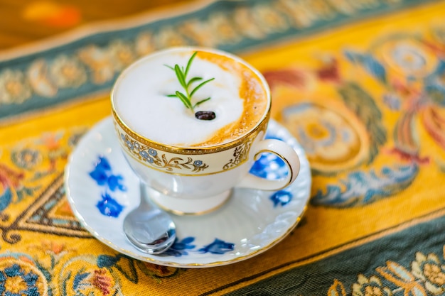 Hot cappuccino in white ceramic cup on the luxury table cloth and wooden table, top view