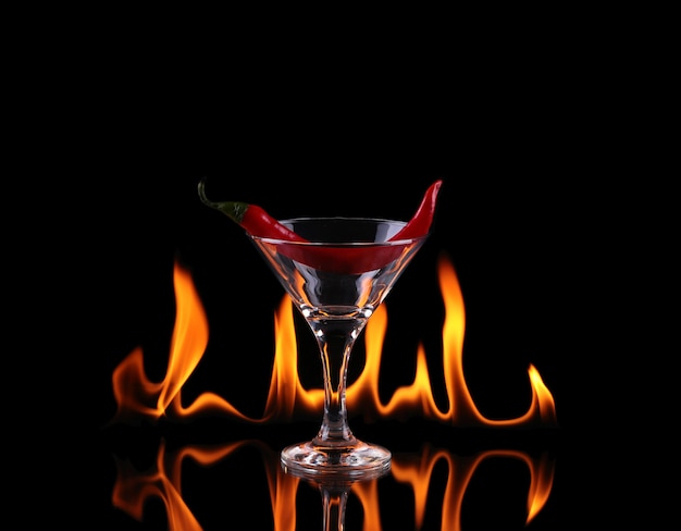 Hot chili peper in een martiniglas met een vuur op een zwarte achtergrond