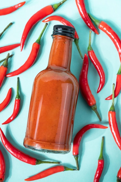 Hot chili sauce in a bottle on a bright blue background with fresh red pepper The concept of vegetarian delicious food