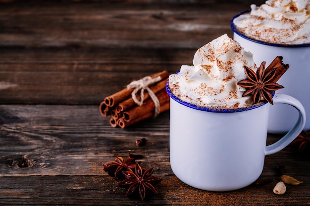 Hot chocolate drink with cinnamon and whipped cream on wooden background