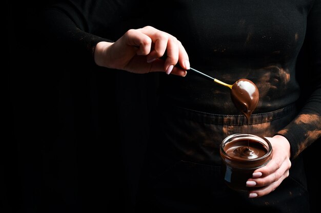 Foto cioccolato caldo mani femminili tengono un cucchiaio con cioccolato fuso utensili da cucina su uno sfondo nero