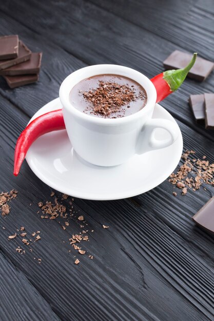 Cioccolata calda nella tazza bianca e peperoncino rosso sul tavolo di legno nero.