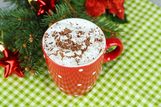 Hot chocolate with cream in color mug, on napkin, on Christmas decorations background