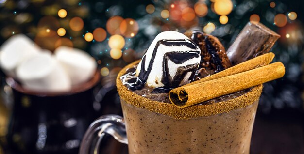 Cioccolata calda con caramelle marshmallow, una tipica bevanda natalizia e festiva, tazza d'oro, luci e decorazioni natalizie, sciroppo di cioccolato gocciolante