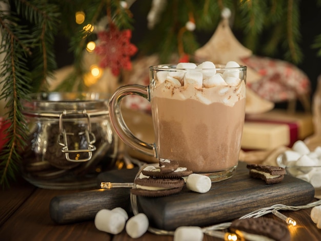 Cioccolata calda con marshmallow in una tazza di vetro su un tavolo di legno sotto l'albero di natale