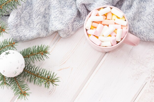 Hot chocolate with marshmallows in a pink cup on a white wooden table.