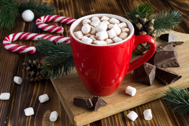 Hot chocolate with marshmallows in the red cup on the wooden cutting board