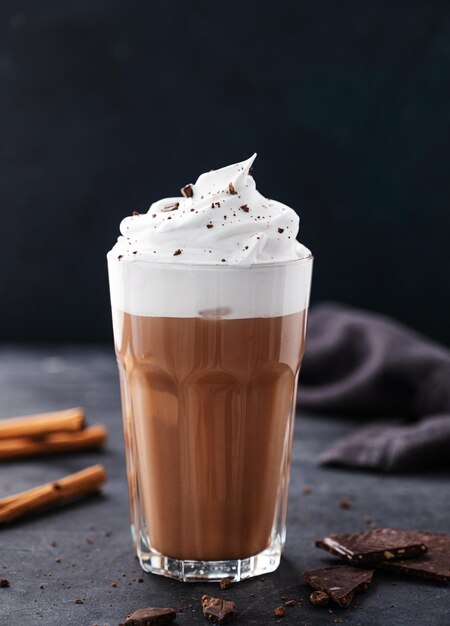 Hot chocolate with whipped cream and cinnamon in a tall glass on a dark background Front view and copy space