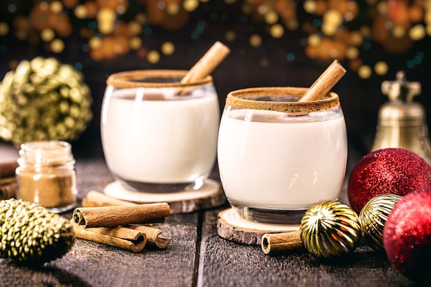 Hot christmas drink with decoration and christmas lights in the background, called eggnog, made with sugar, nutmeg, cinnamon and alcoholic drink