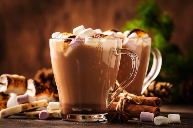 Hot cocoa or chocolate drink with marshmallow in glass mug and winter decoration on wooden table Concept of cosy Christmas and New Year holidays copy space