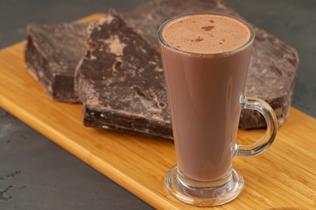 Hot cocoa drink in glass cup and chocolate bar on gray background close up