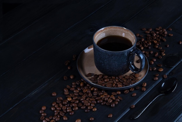 Hot coffee in beautiful blue coffee mug surrounded by coffee beans on dark wooden table