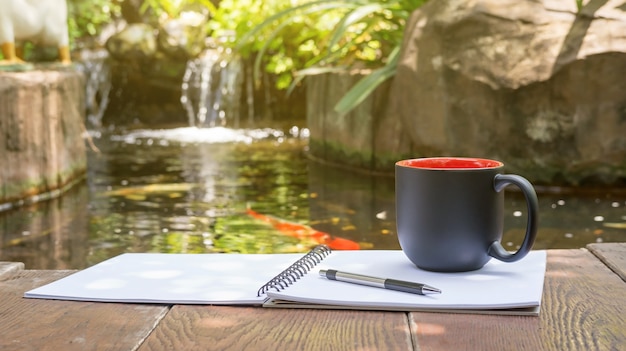 Hot coffee, book, and pen place near a fancy carp pond.