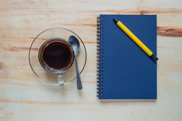 Hot coffee and book with pen on wood table