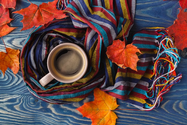 Hot coffee cappuccino, blanket and autumn leaves on old wooden surface