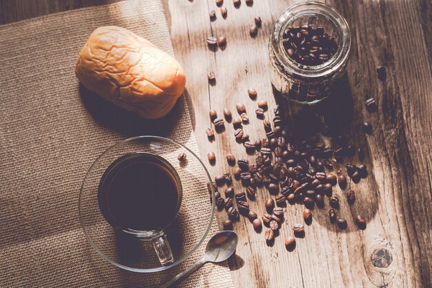 Hot coffee in a clear coffee cup and coffee beans on old wooden in a warm light on top view