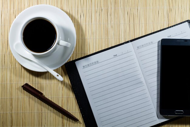 Hot coffee cup with notebook and mobile on the desk businessman