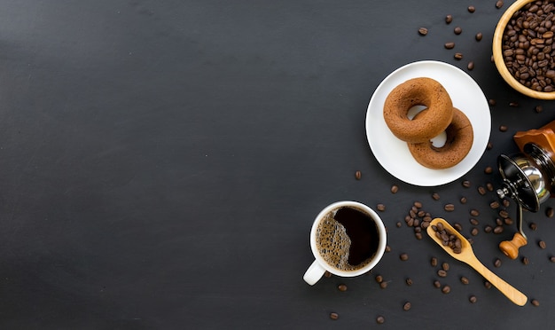 Hot coffee, donuts, bean and hand grinder on black table 