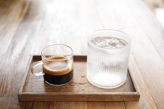 Hot coffee and glass of ice on wooden tray on wooden table