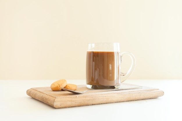 Foto cappuccino al latte caldo in bicchiere di caffè trasparente su sfondo beige con cucchiaio e fagioli arrostiti