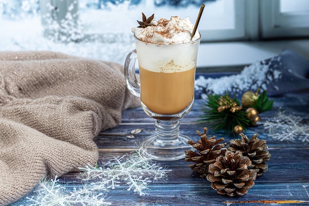 Hot coffee latte with cinnamon sticks, sprinkled with cinnamon. Christmas decorations, branches of a Christmas tree. Holiday concept New Year. On a wooden background.