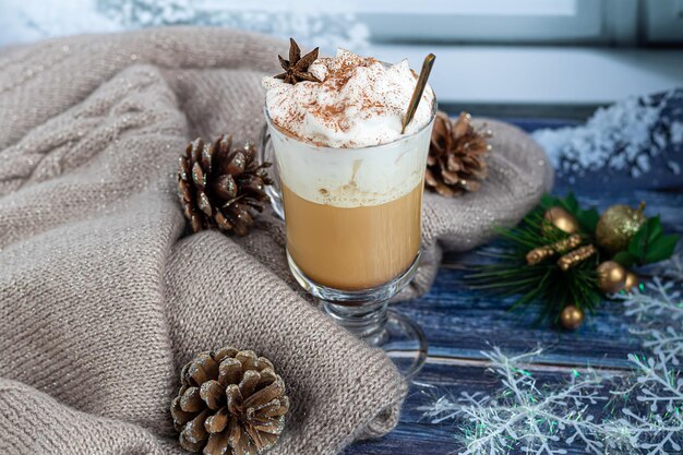 Hot coffee latte with cinnamon sticks, sprinkled with cinnamon. Christmas decorations, branches of a Christmas tree. Holiday concept New Year. On a wooden background.