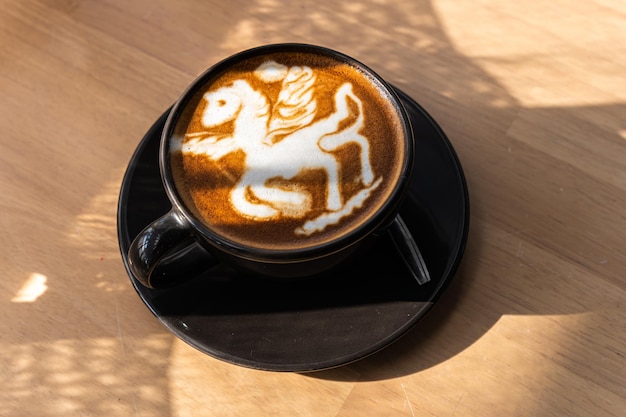 Hot coffee latte with latte art in the form of a horse milk foam in cup mug on wood desk on top view As breakfast In a coffee shop at the cafeduring business work concept