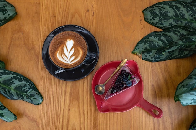 Latte caldo al caffè con schiuma di latte art in tazza e torta di mirtilli sulla scrivania di legno in vista dall'alto come colazione in una caffetteria al bar durante il concetto di lavoro aziendale