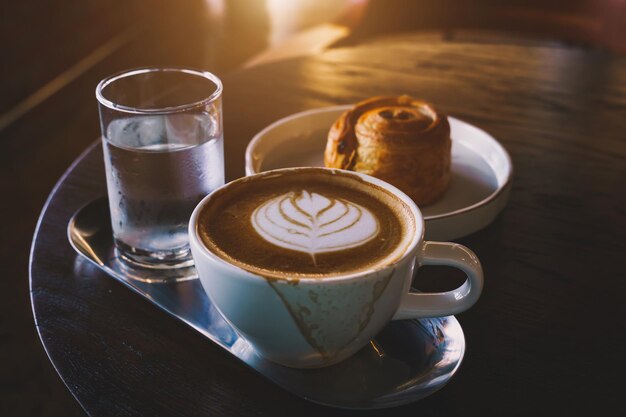 Hot coffee latte with latte art milk foam in cup mug and Homemade Raisin Danish white plate on wood desk on top view As breakfast In a coffee shop at the cafeduring business work