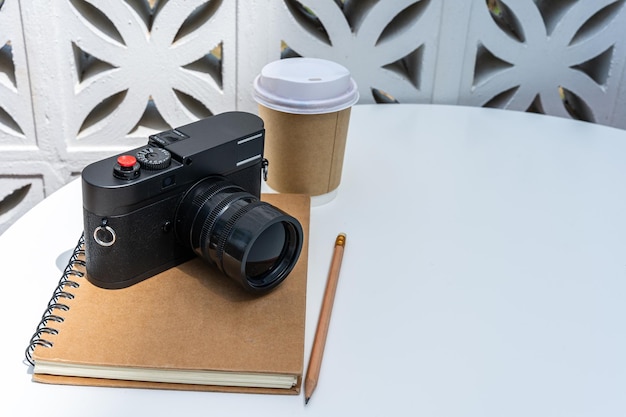 Hot coffee latte with latte in cup made of paper and camera in notebook on white wood table desk on top view As breakfast In a coffee shop at the cafeduring business work concept