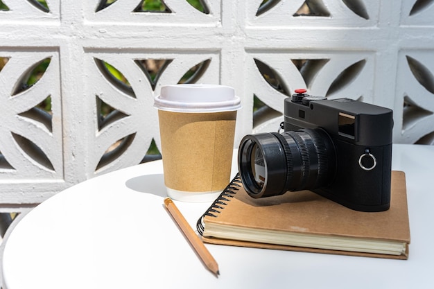 写真 紙で作られたカップにラテを入れたホットコーヒーラテと、ビジネスワークコンセプト中のカフェの喫茶店での朝食として、白い木のテーブルの上にノートにカメラ