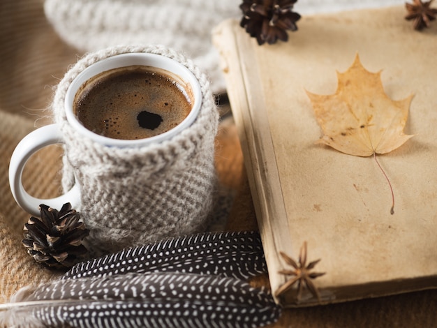 Hot coffee in a mug on a plaid and a knitted scarf. Cozy home morning with a book