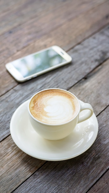 Hot coffee and smartphone on a wooden table.