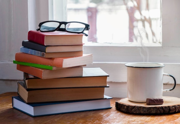 Hot coffee or tea cocoa chocolate cup on book and eyeglasses with copy space for text against the background of a bookshelf