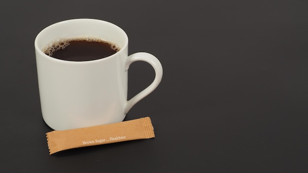 Hot coffee in white cup and brown sugar sachet isolated on black blackground.