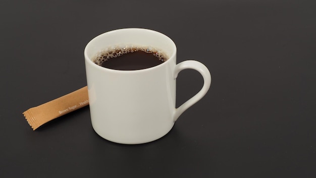 Горячий кофе в белой чашке и пакетике с коричневым сахаром на черном фоне