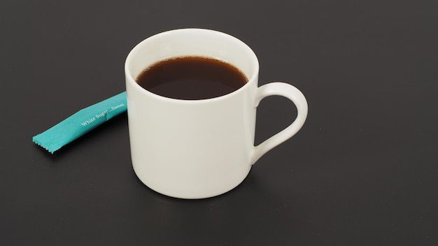 Hot coffee in white cup and white sugar sachet on black blackground