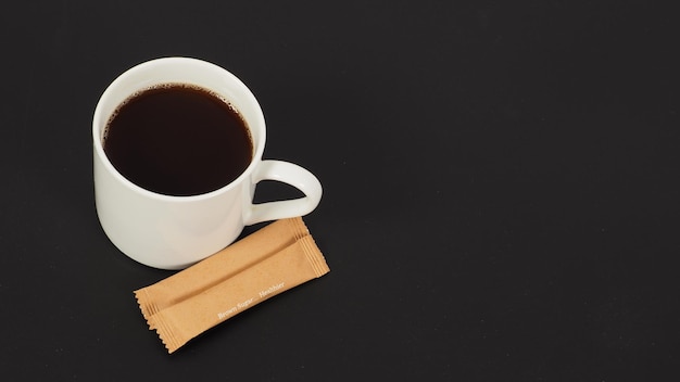 Hot coffee in white mug and two brown sugar sachet isolated on black blackground.