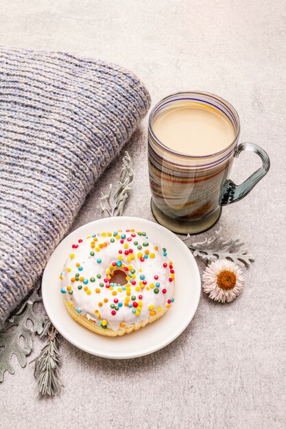 Hot coffee with a donut. Winter drink for a good mood with sweater, leaves and flowers.