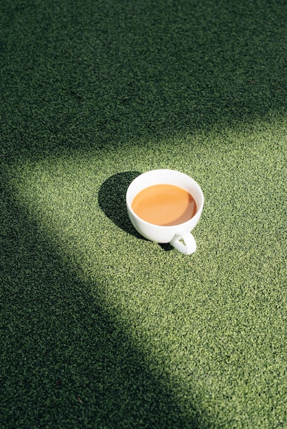 A hot cup of coffee on a cold morning, on green grass with dew background