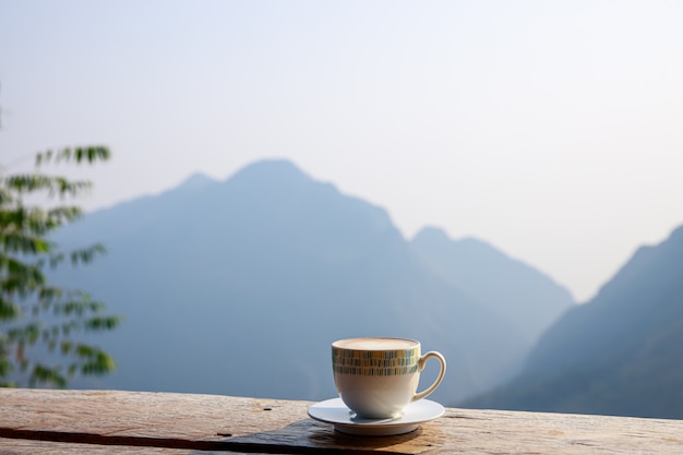 木製のテラスと山を背景に熱い一杯のコーヒーを配置します。