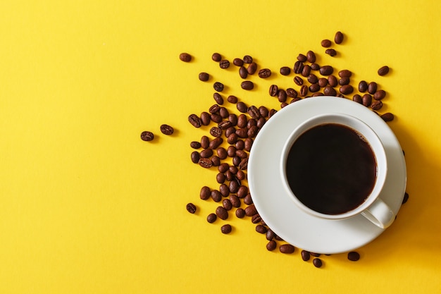 Tazza di caffè caldo con fagioli sparsi su uno sfondo giallo