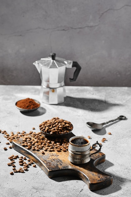 Hot cup of espresso with coffee beans scattered on wooden board and a pot under hard morning sun