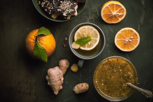 Hot cup of green tea with lemon,ginger,confiture on black surface,top view