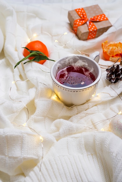 Hot Cup of tea with tangerines and sweaters on bed