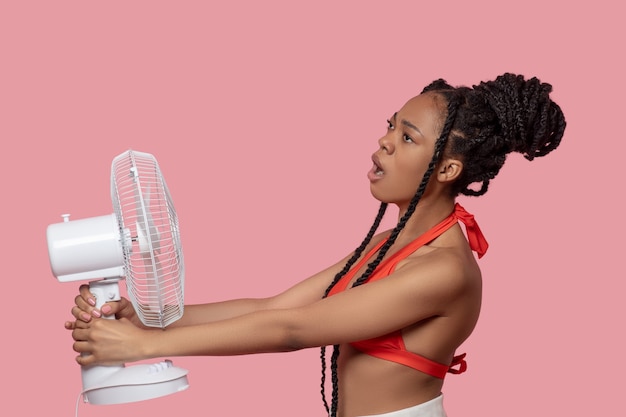 Hot days. Smiling african american woman holding a fan looking tired from heat