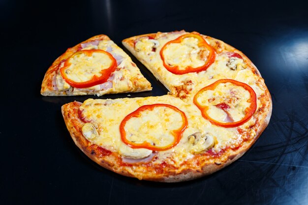 Hot delicious homemade American pizza with red pepper and meat with a thick crust on a black table